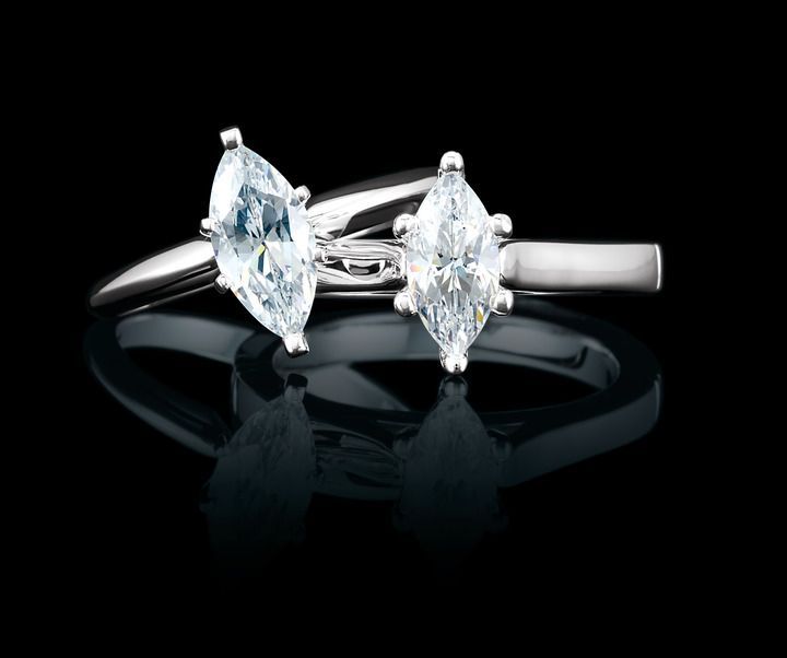 Two marquise diamond rings on black reflective surface